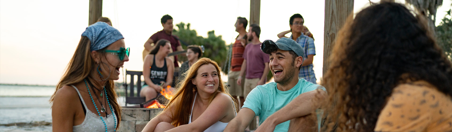 Eckerd students laughing together around a fire bit by the beach