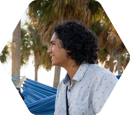 Student with long hair smiles while seated near hammock and palm trees
