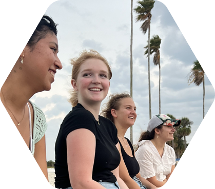 Students seated outside with palm trees behind them