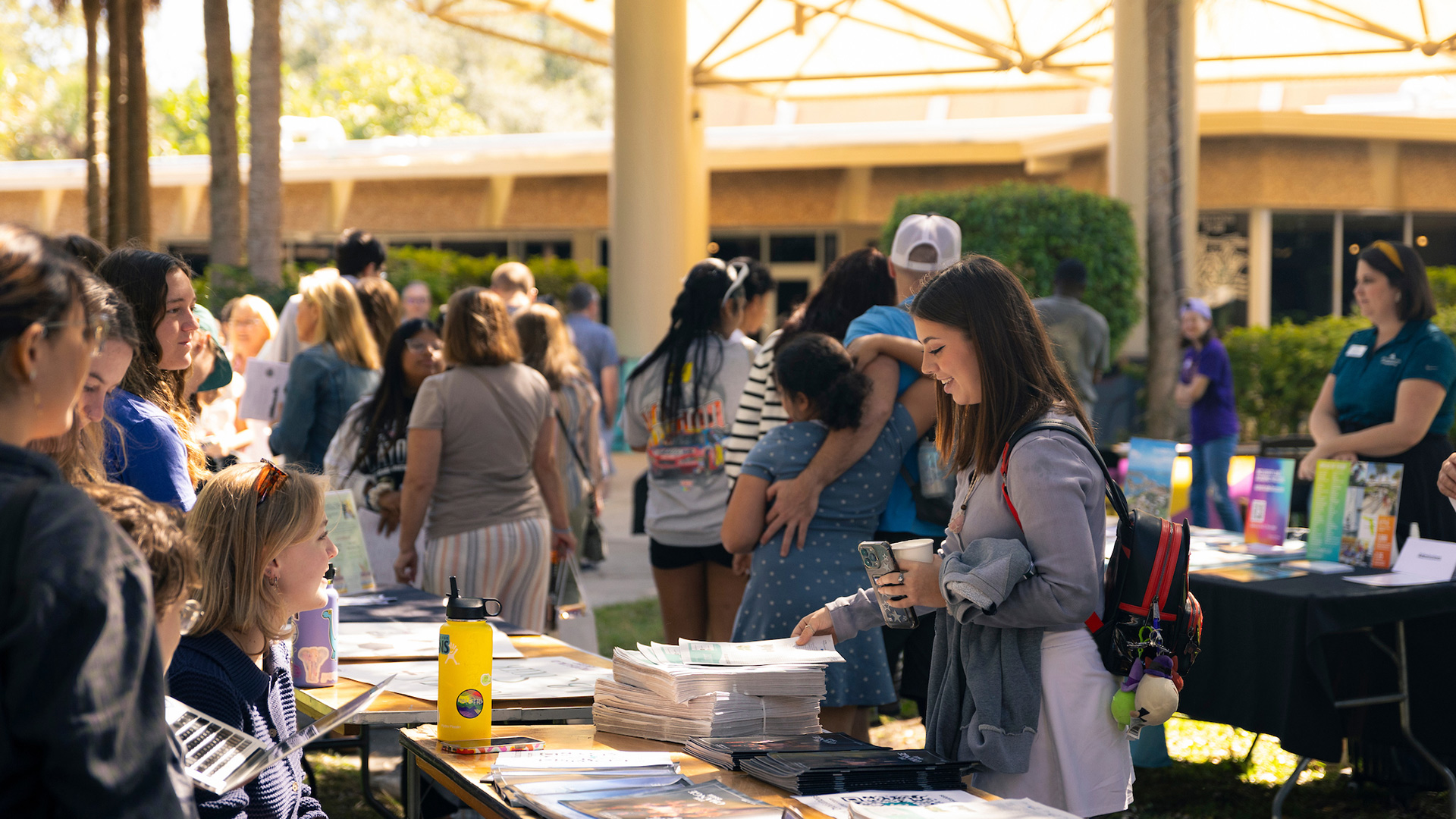 Students sit at table booths outside with families milling about