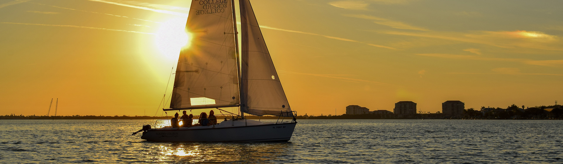 Sailboat with "Eckerd College" text on the sails glides over the water at sunet