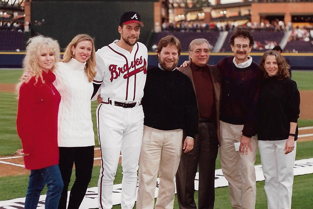 Six people stand with Braves baseball pitcher Smolz in stadium