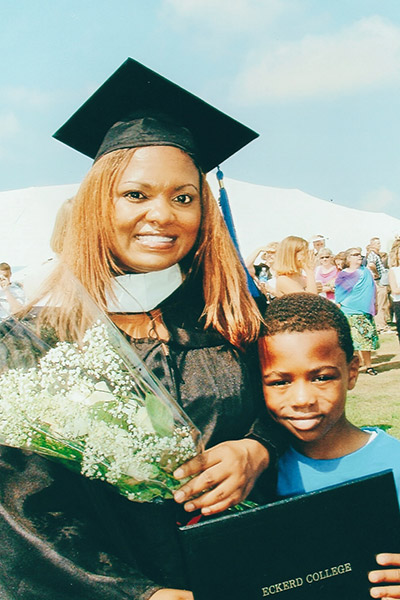 Graduate in cap, holding flowers with young son holding her degree
