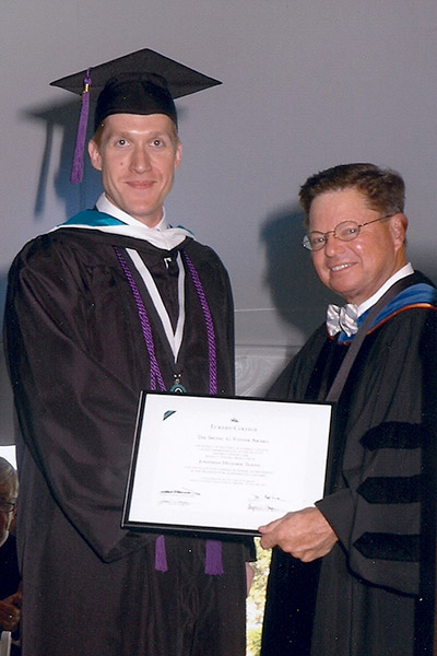 Young man in graduation cap receives diploma from college president