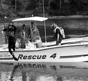 Black and white photo of divers in scuba gear diving off of a boat labeled "Rescue 4"