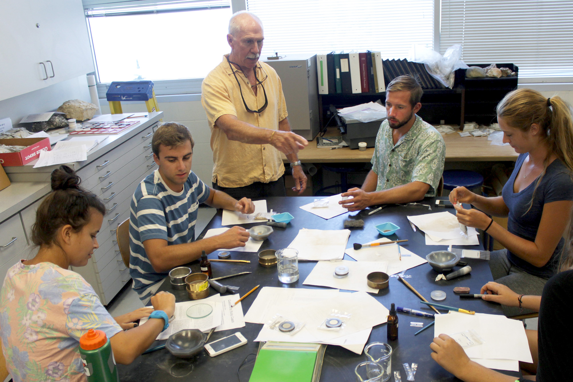 Four students at a lab table while professor stands alongside