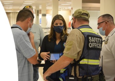 Woman in a small huddle of people wearing masks, one person with a vest that reads SAFETY OFFICER