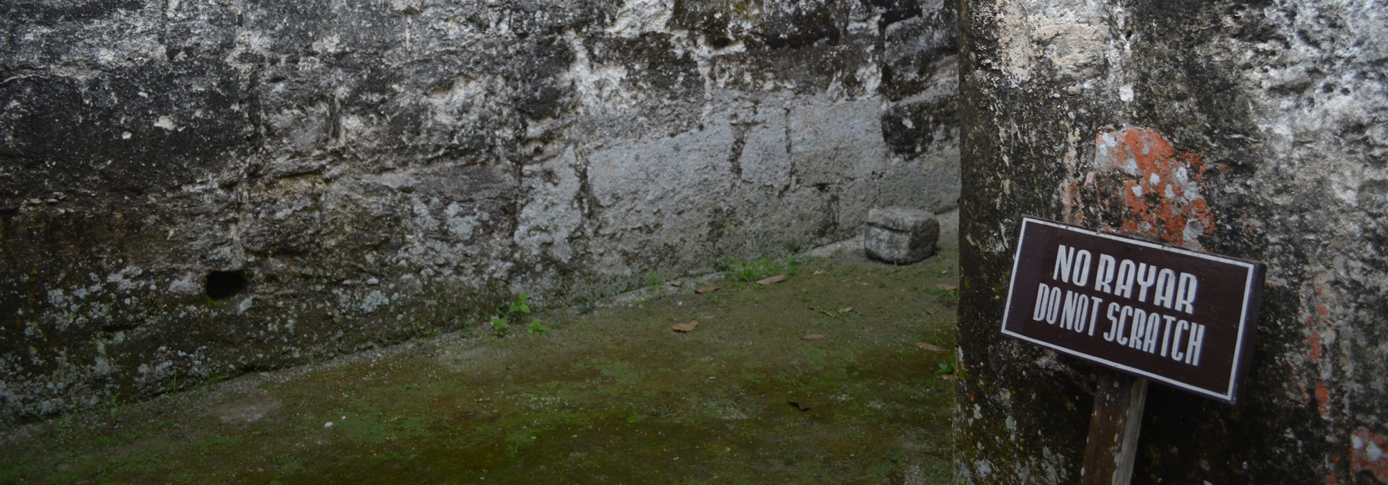 Stone ruins in Tikal, Guatemala that was abandoned during the 10th century AD with a sign that says "Do not scratch" in Spanish and English
