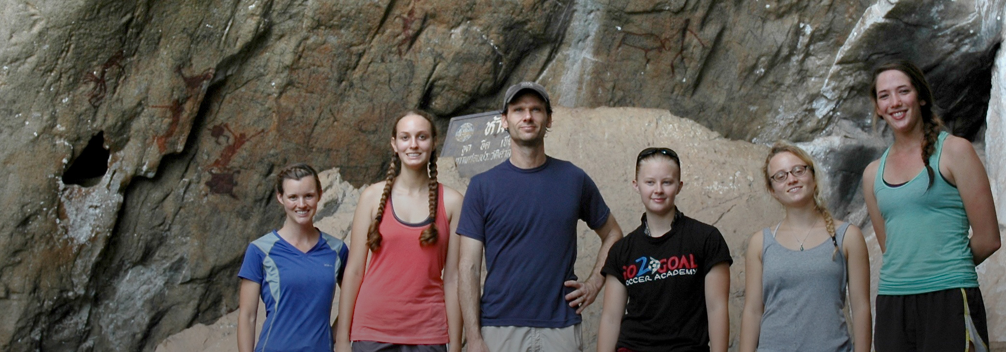 Anthropology Professor Scott Burnett stands with students in front of a waterfall and rock art in Thailand.
