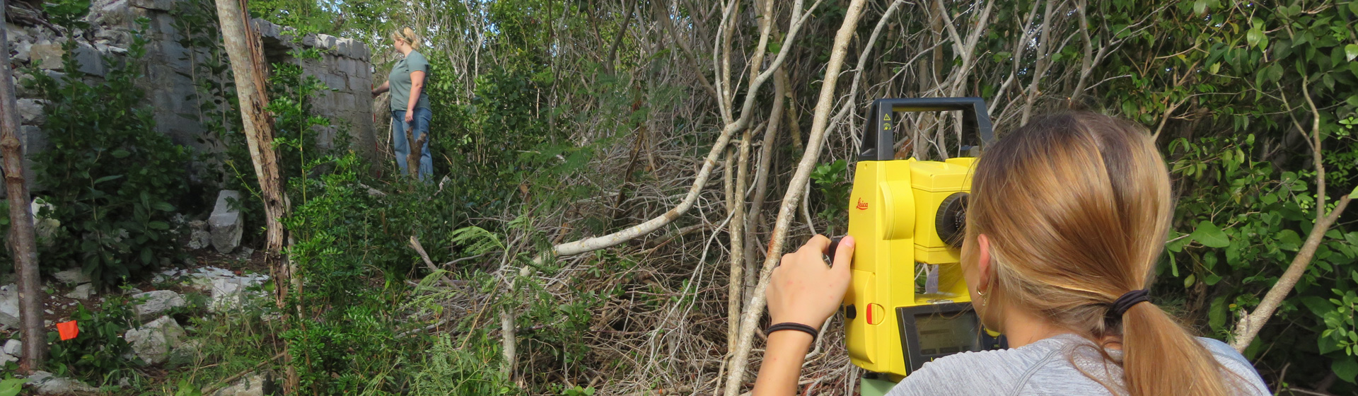Student using equipment in the field in a jungle setting with an old building in the background