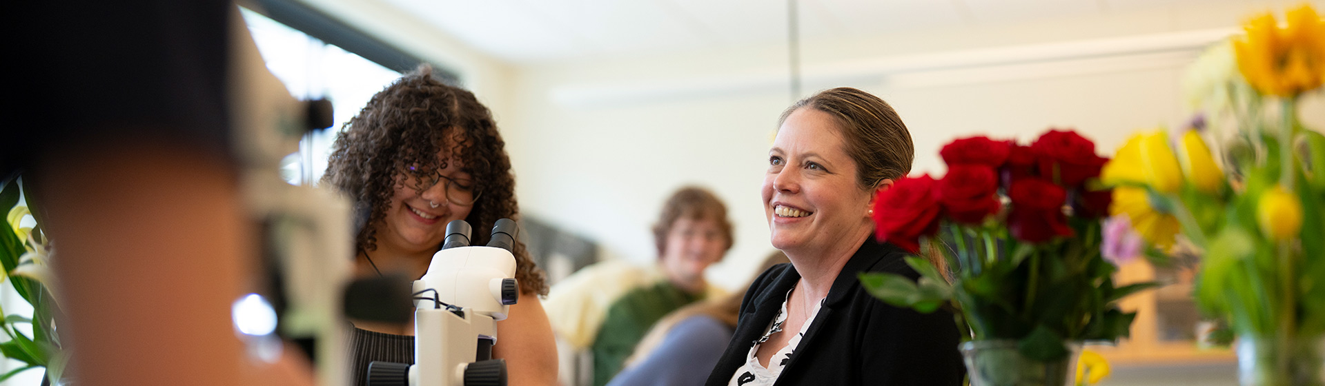 Student and professor smile together at a lab table with flowers around them