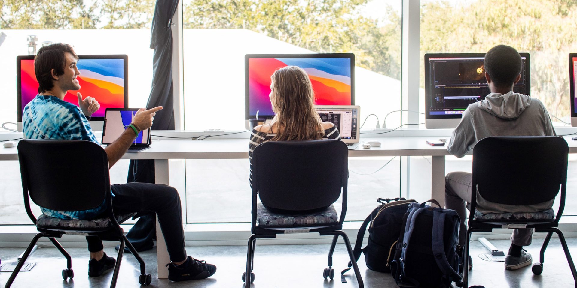 Three students seated in front of large computers