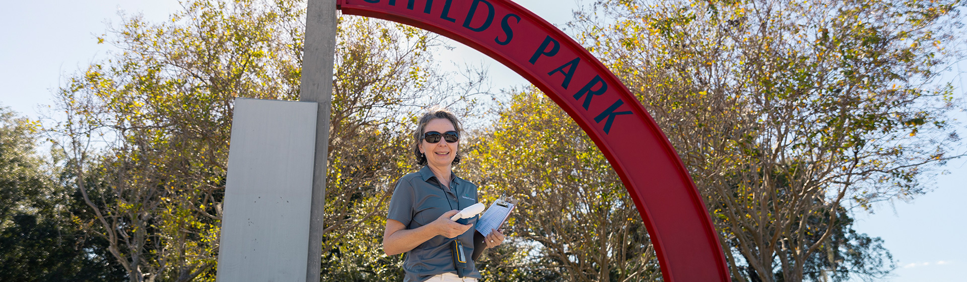 Professor stands outdoors below a sign that reads PARK while holding air sampling equipment