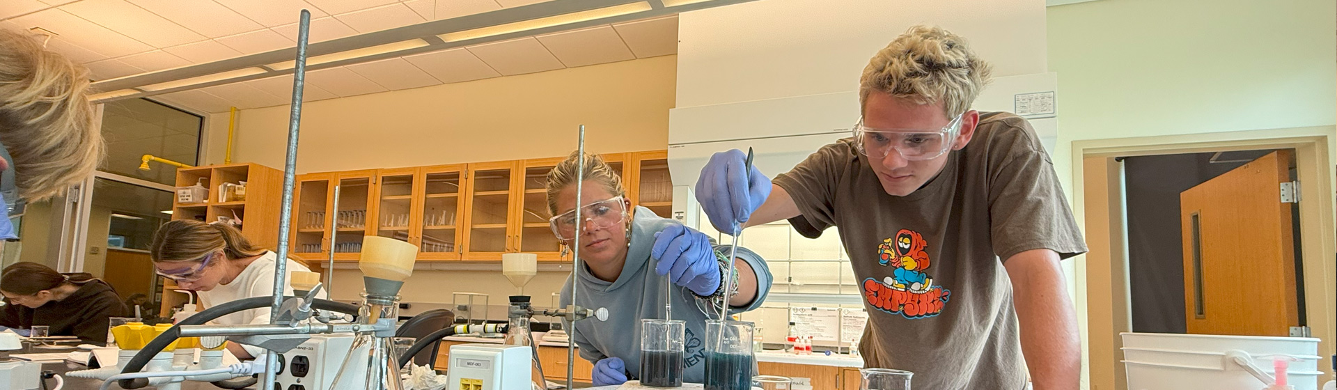 Two students wearing goggle conduct chemistry experiment in a lab