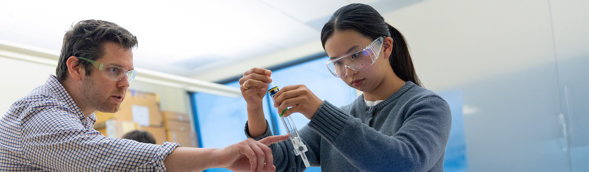 Professor and student in protective eyewear look at a chemistry sample together