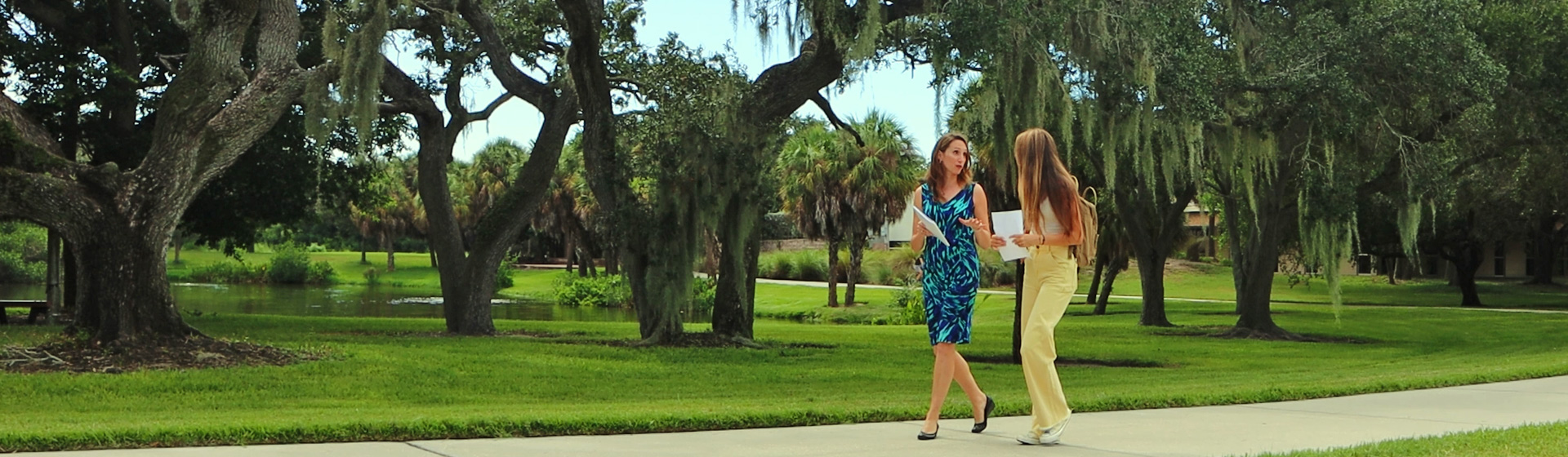 Professor and student discuss communication while walking across a lush campus