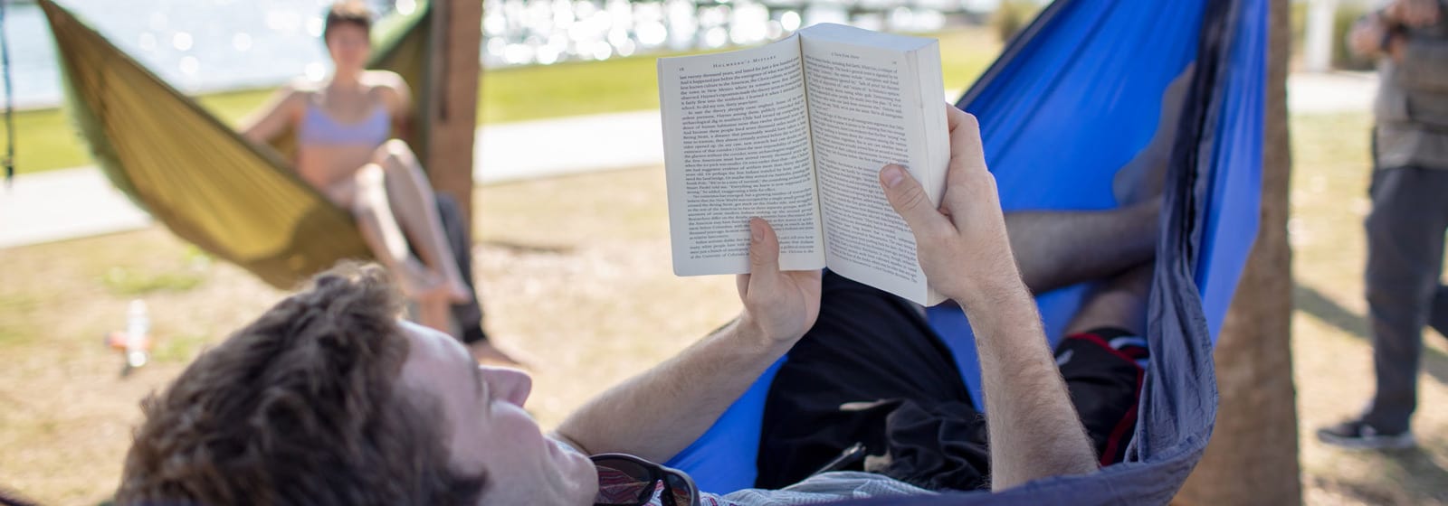 Student reading a book in a hammock on the beach