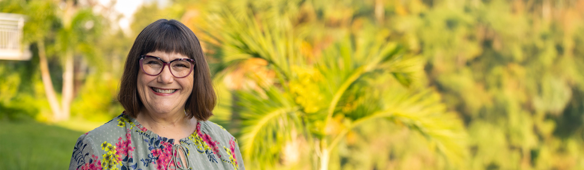 Professor in glasses stands in front of lush, tropical environment
