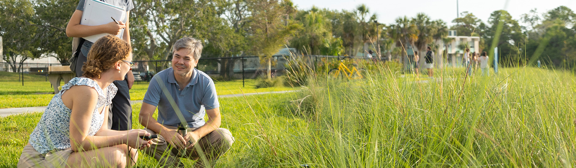 Student and professor squat in native grasses along a shoreline