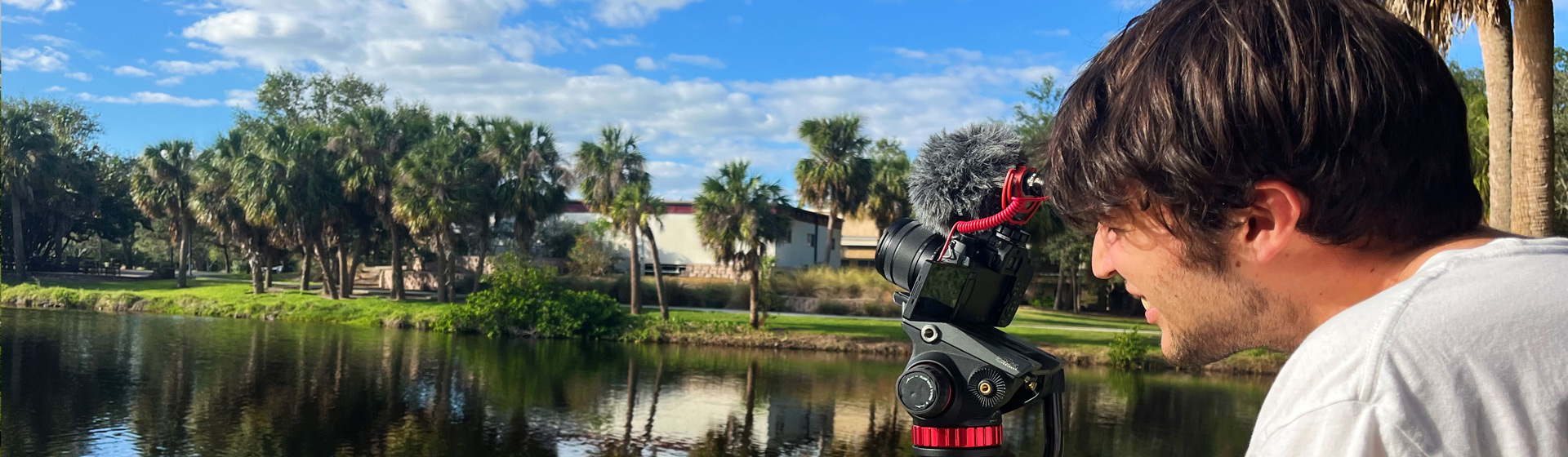 Student stands behind tripod and camera while surveying a pond