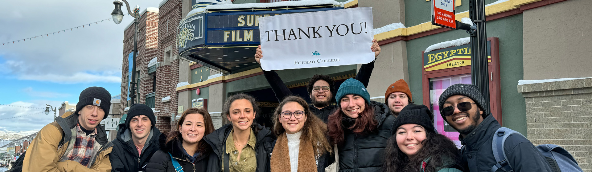 Group of students in warm weather stand together smiling on a street in a small town