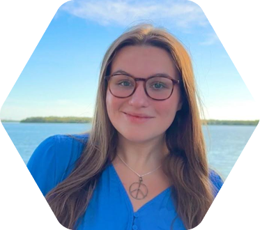 Young lady wearing glasses and peace necklace stands outside in front of a bay