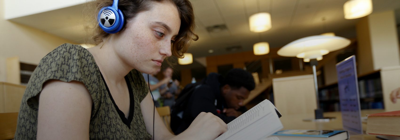 Student wearing headphones reading at table in library