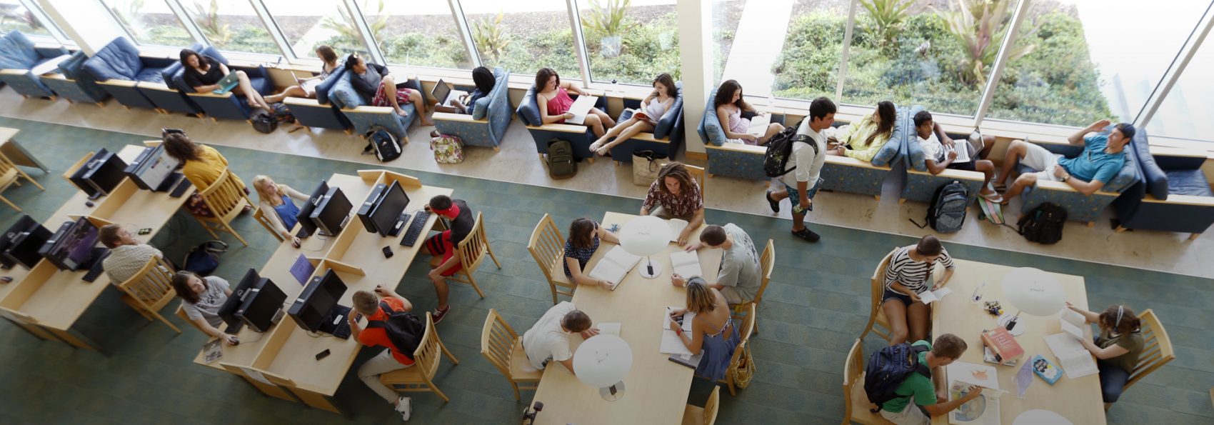 Overhead shot of students sitting in armchairs and at tables in Armacost library.