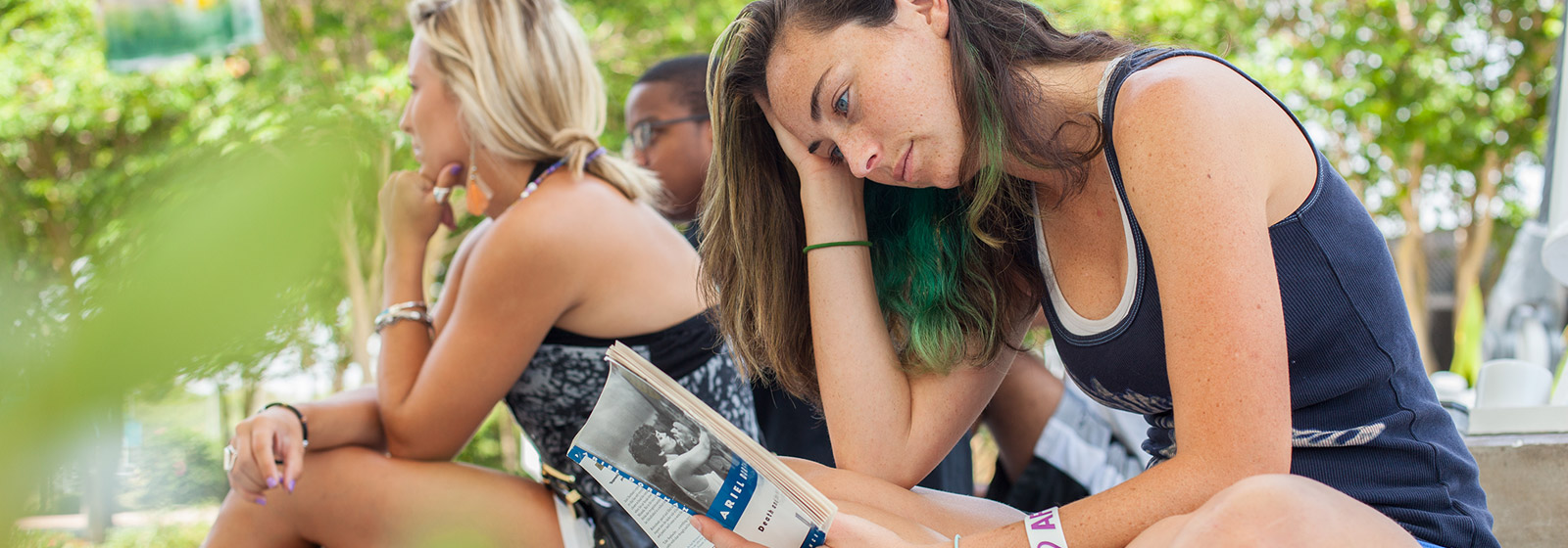 Student with green hair reading literature outdoors