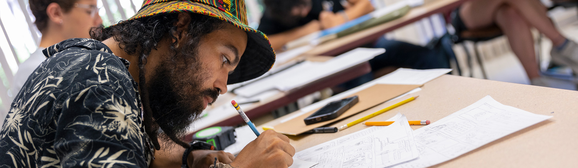 Student with beard and nose ring leans over paper with pencil