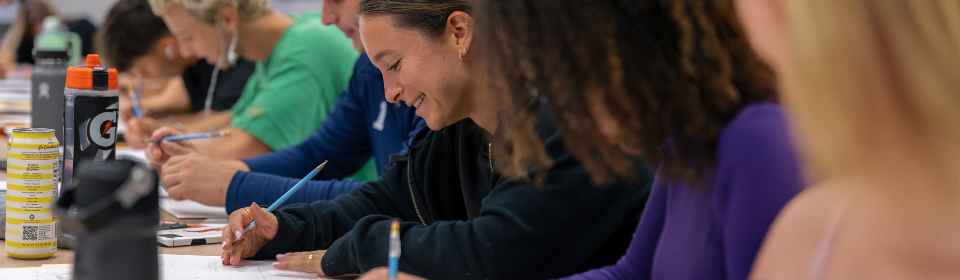Students smiling side by side writing with pencil and paper