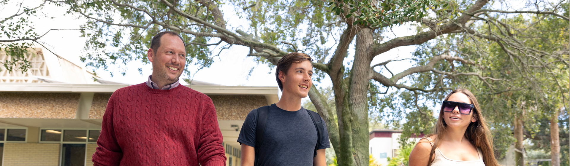 Professor walking down path with two students while smiling