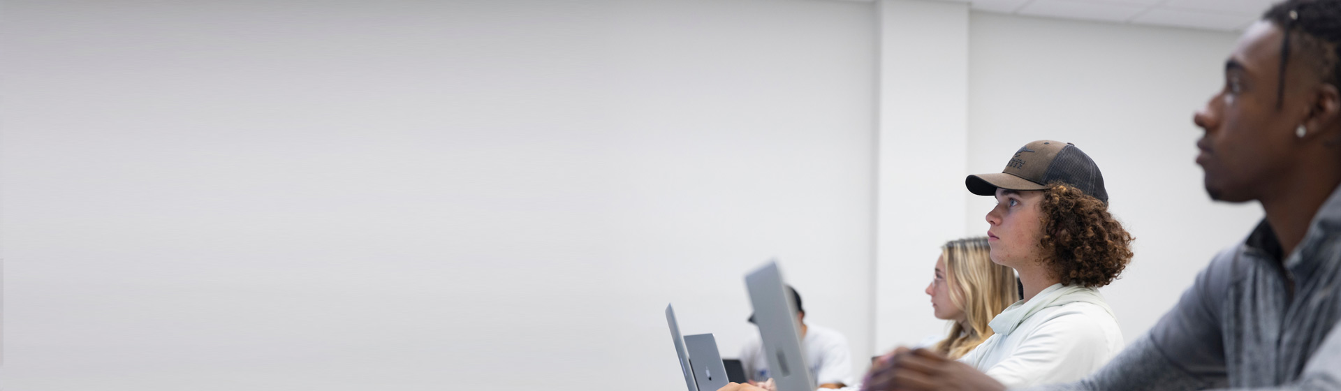 Three students seated at computers face the front of a classroom
