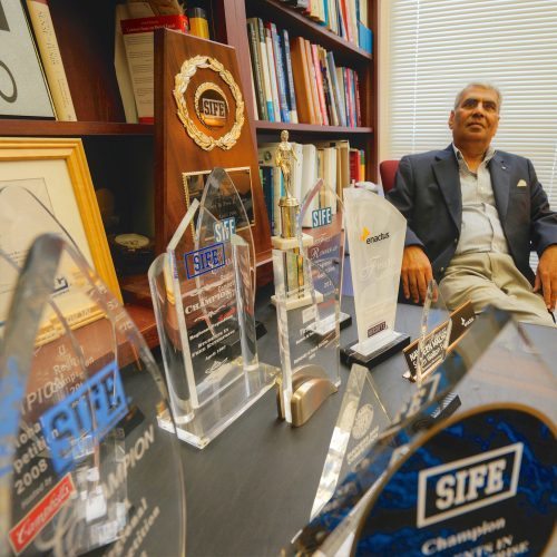 Dr. Malhotra sits in his office with numerous SIFE awards on his desk.