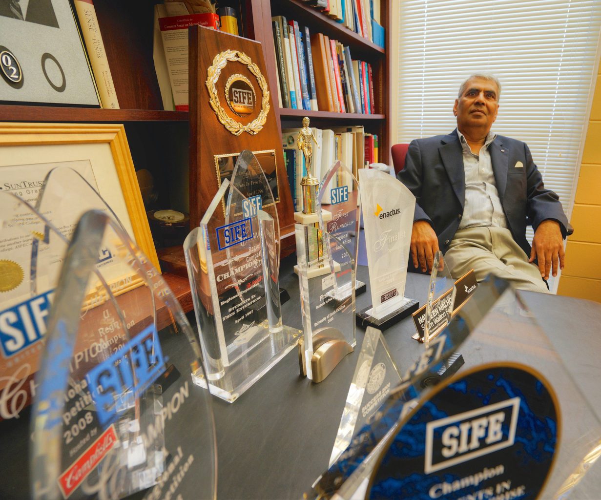 Dr. Malhotra sits in his office with numerous SIFE awards on his desk.