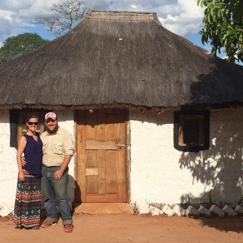 Couple standing out of a simple home in Zambia