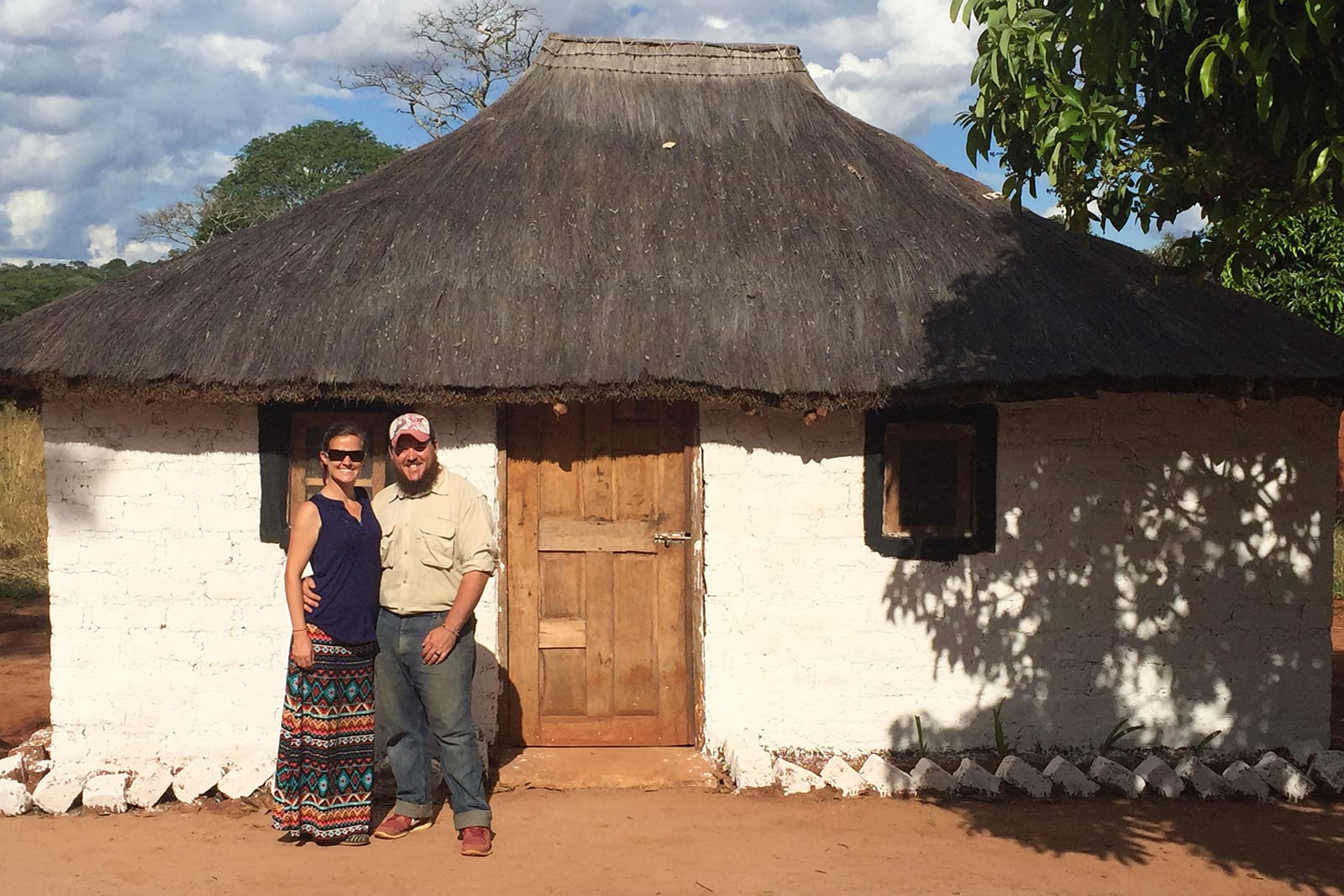 Couple standing out of a simple home in Zambia