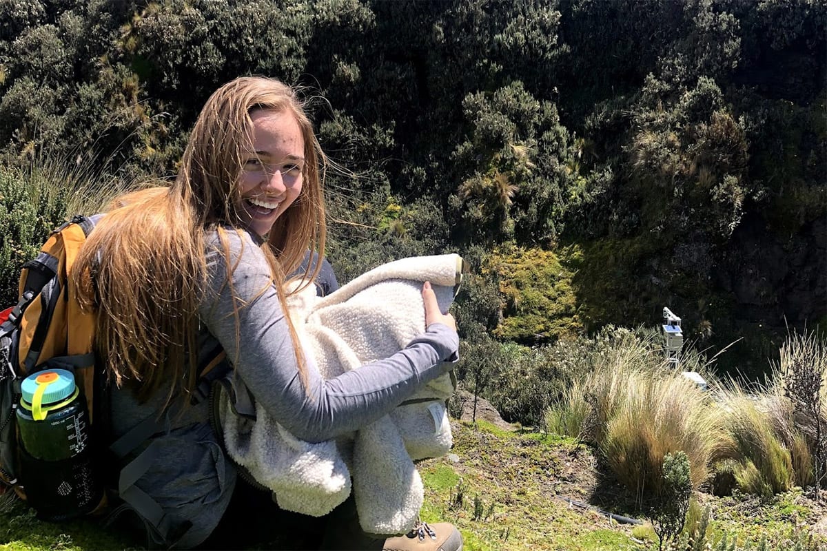 Student seated on side of ravine in forest