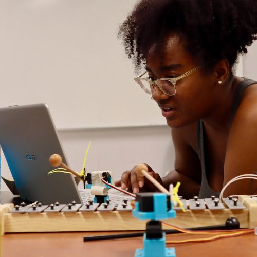 Female student working on computer next to xylophone