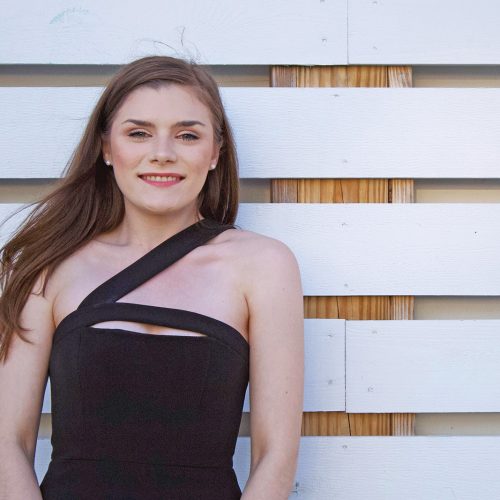 Eckerd College business student in formal attire in front of wooden fence