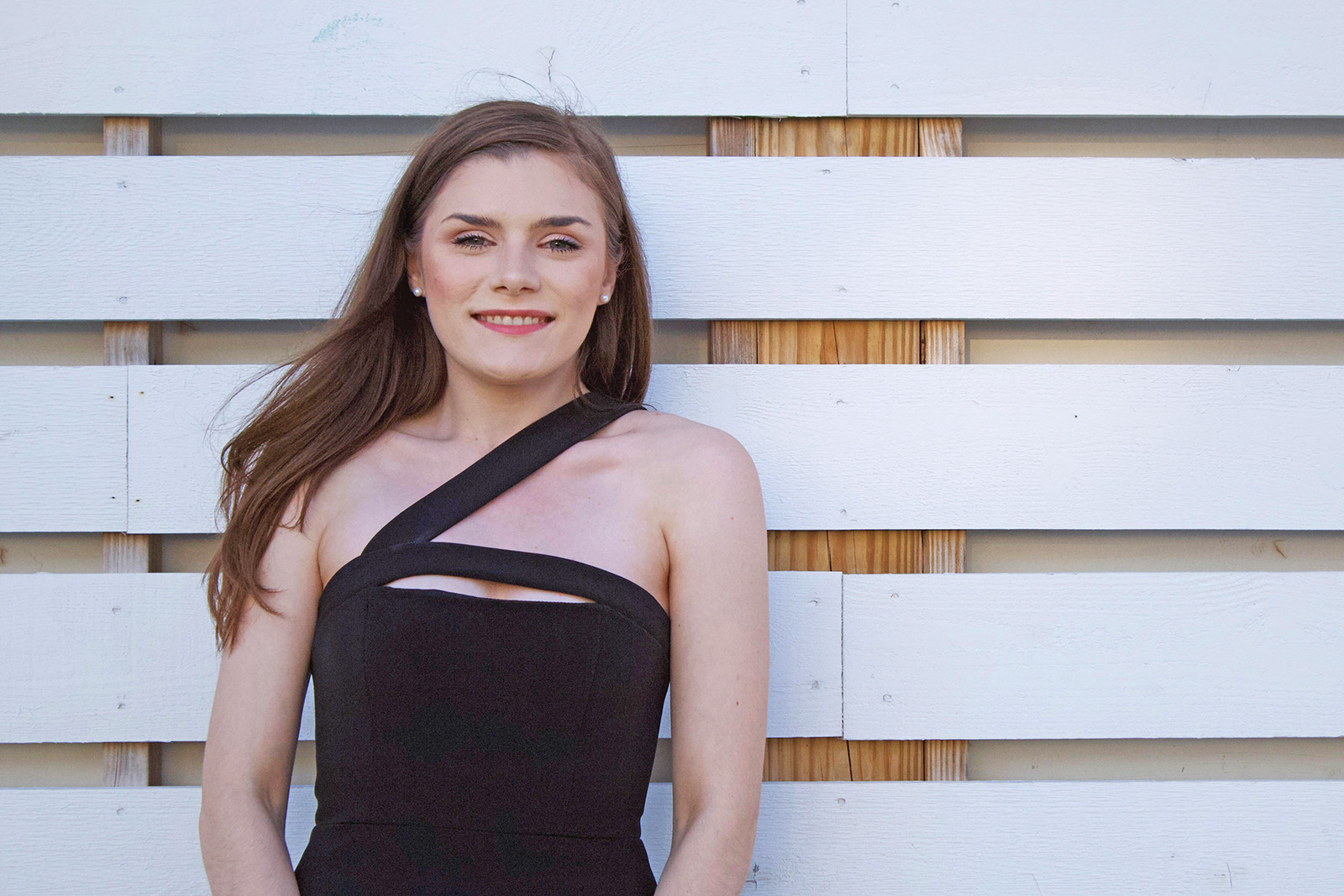 Eckerd College business student in formal attire in front of wooden fence