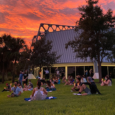 Eckerd College first-year students sit by chapel under a vibrant sunset