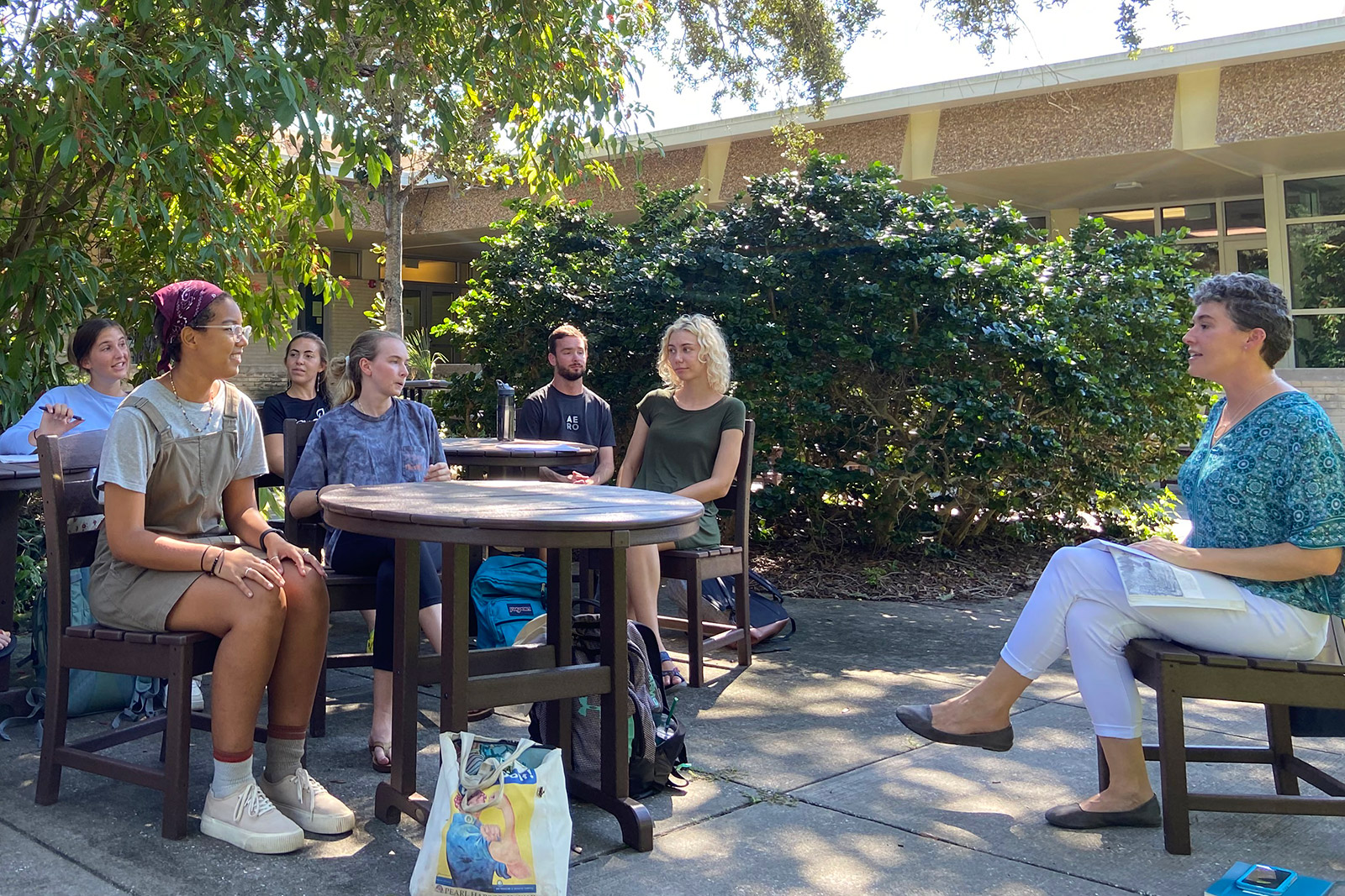 Professor seated outside with a class of students seated at round tables