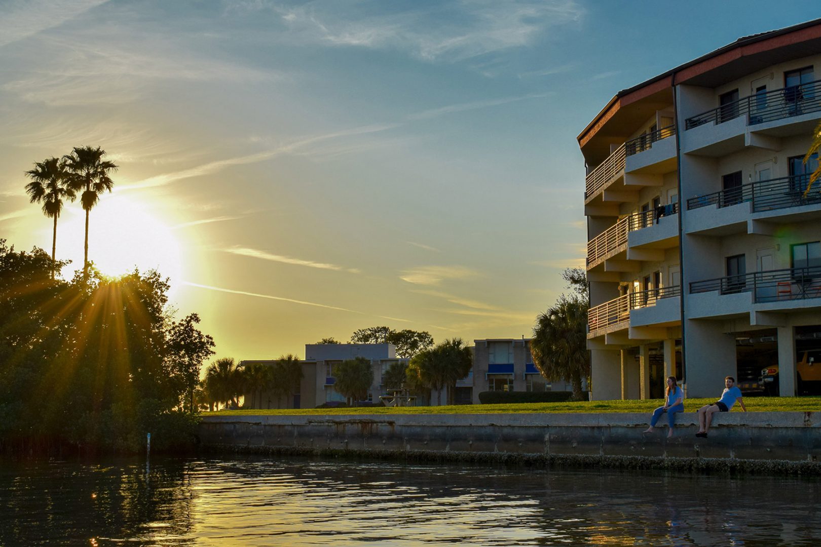Students sit along the seawall next to the Omega residence hall at Eckerd College