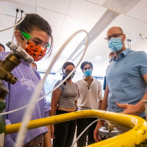 Students wearing goggles look at equipment as Joe Larkin oversees the activity