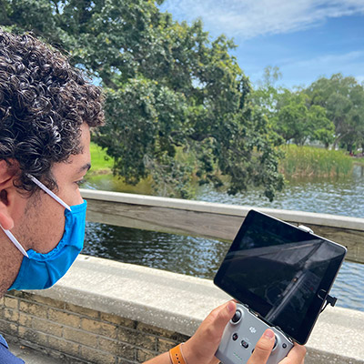 Student looking at controls for drone flying over Fox Pond