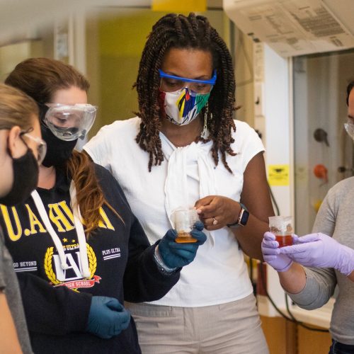 Eckerd College chemistry professor stands with students, looking at beaker of chemicals