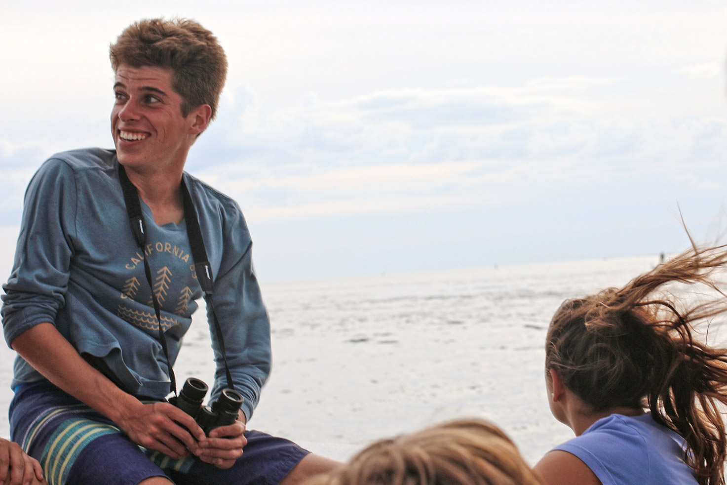Eckerd student on edge of boat holding binoculars