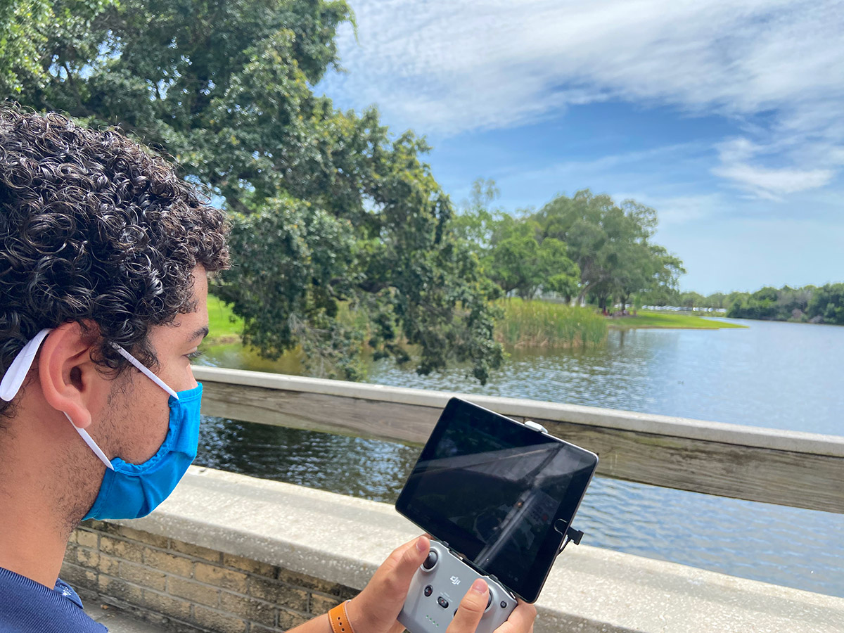 Student looking at controls for drone flying over Fox Pond