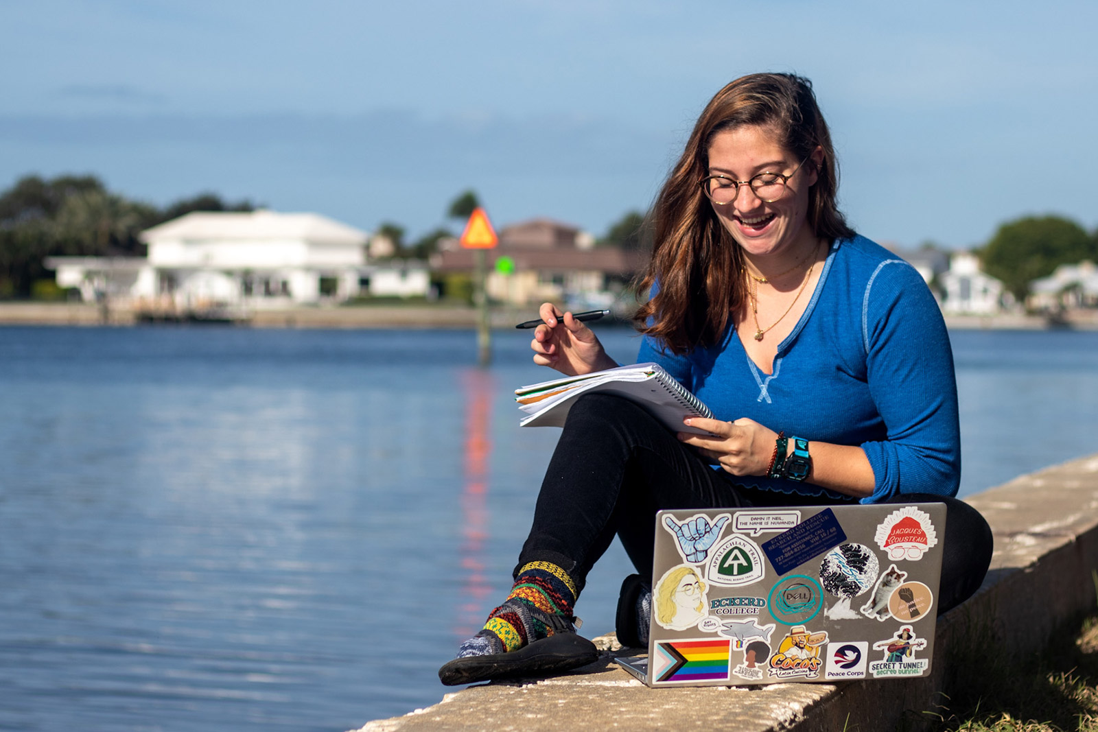 Student writing in notebook next to laptop on seawall
